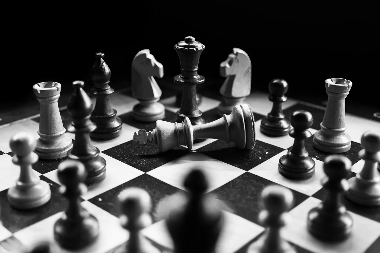 Black and white chess pieces arranged around a fallen king